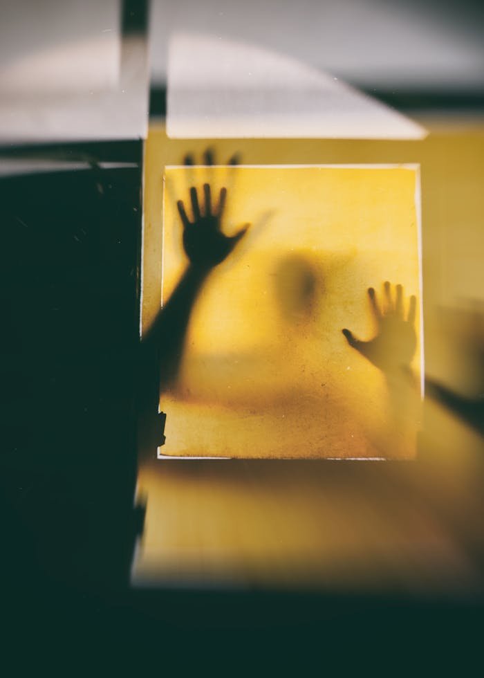 heros-img Eerie silhouette of a person with hands pressed against a yellow surface, creating a suspenseful vibe.